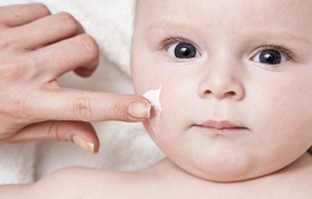 Adult hand is applying cream on baby´s face.