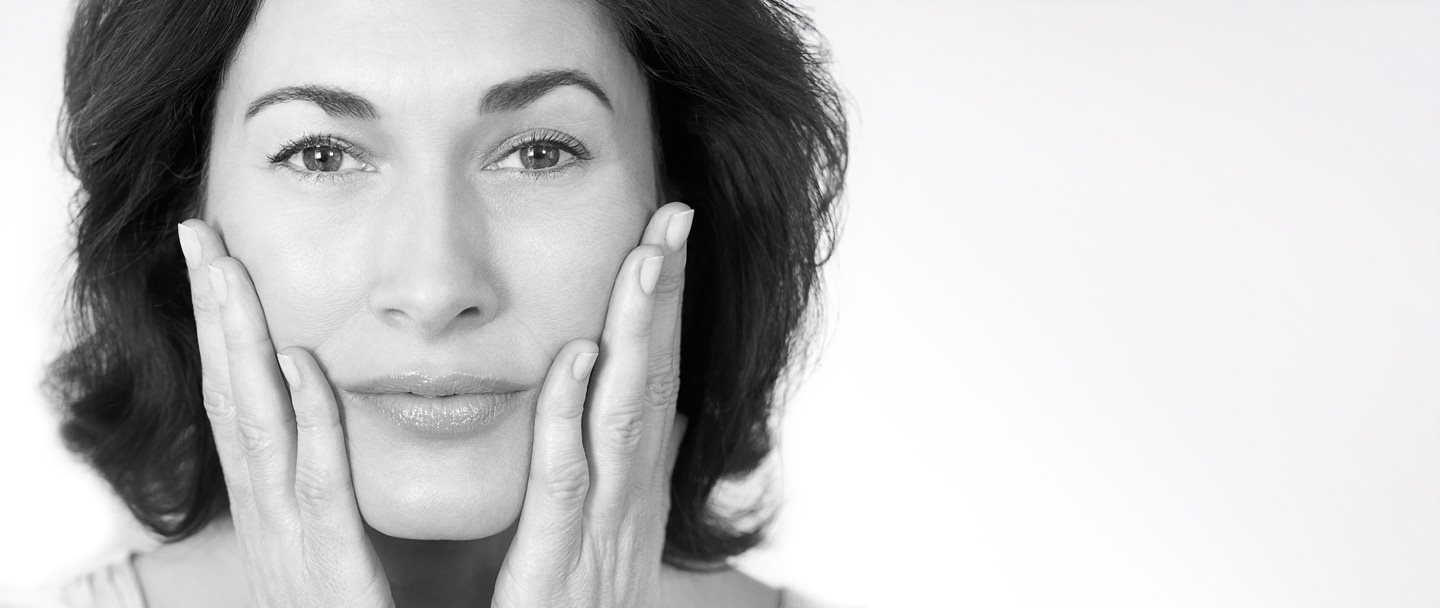 Middle-aged woman touching her cheeks with both hands.